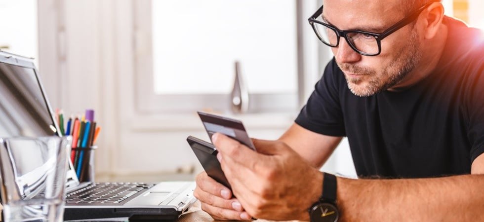 Man in black shirt and glasses staring intently at his credit card