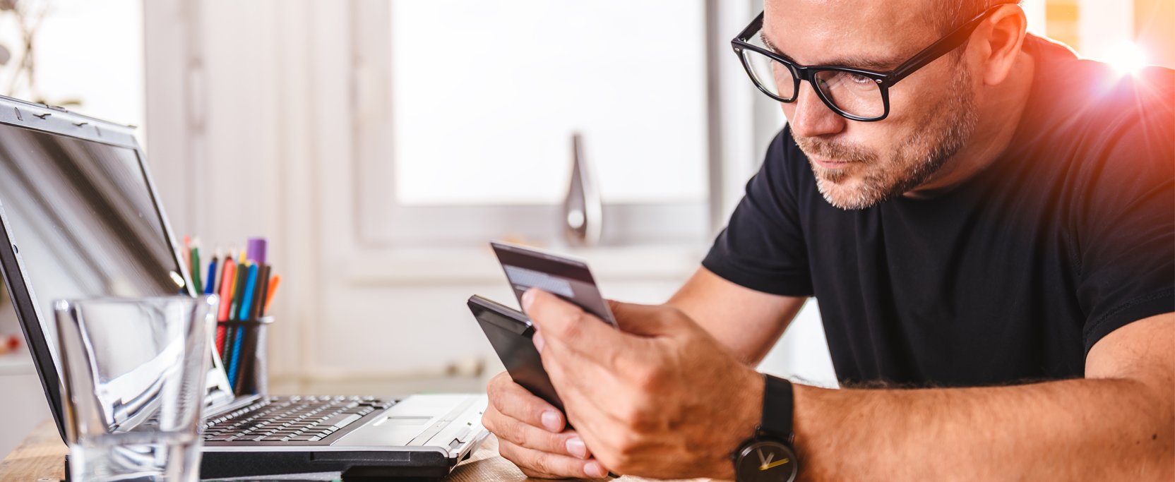 Man in black shirt and glasses staring intently at his credit card