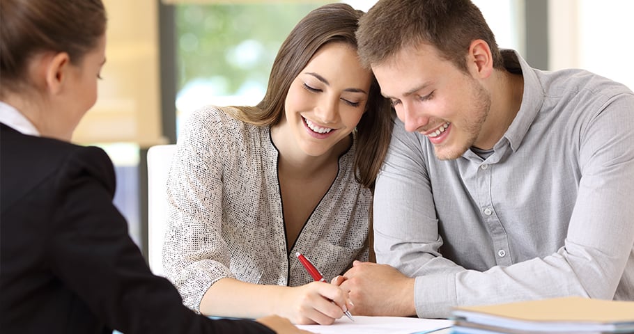 a couple happily signing a contract with a red pen while sitting across from a woman in a suit