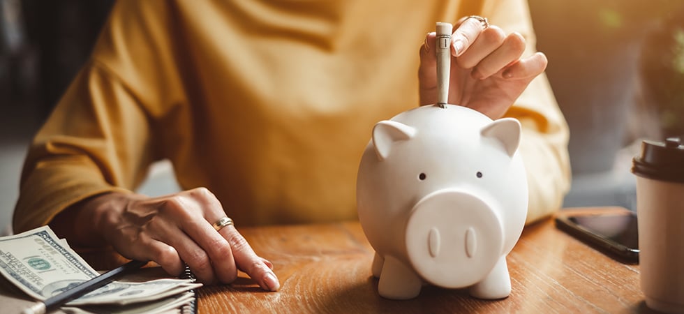 Person sitting at a desk placing rolled up dollar bills into a piggy bank