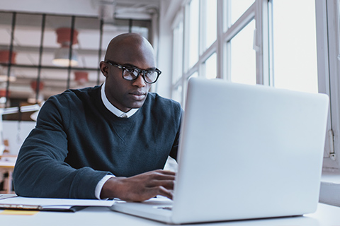 Man in sweater and glasses sitting and typing at a laptop computer