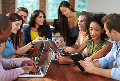 8 colleagues smiling and laughing while working at a shared table