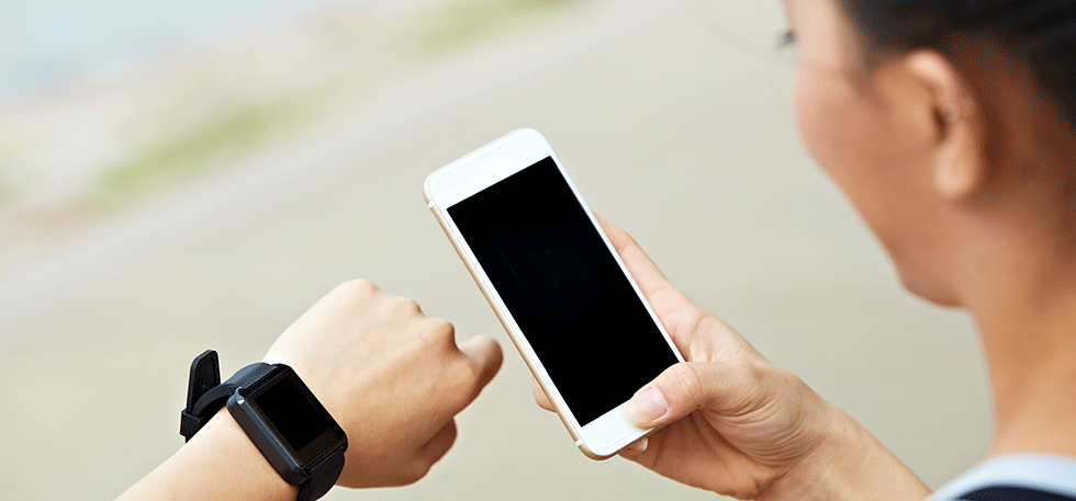 Woman looking at her black smart watch and white smart phone