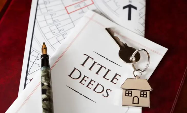 Key and House Keychain Laying on Top of Title Deeds Document